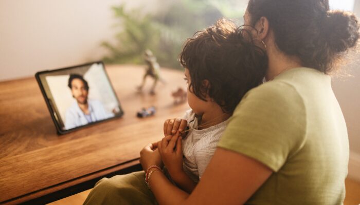 Mother and child video calling their family doctor on a digital tablet. Mother and son having an online consultation with their paediatrician. Loving young mother caring for her sick son at home.